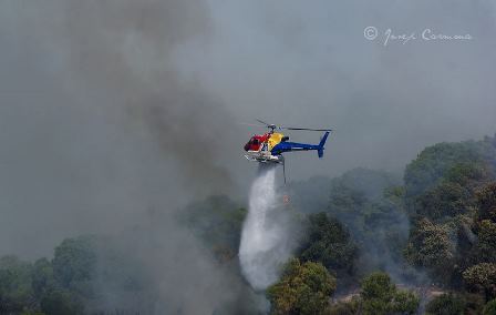 Un helicóptero equipado con un deposito ventral descarga agua en el incendio / Foto: Josep Carmona